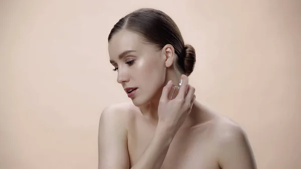 Mujer joven con hombros desnudos sosteniendo botella con perfume de lujo aislado en beige — Stock Photo