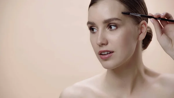 Young woman with bare shoulders holding eyebrow brush isolated on beige — Foto stock