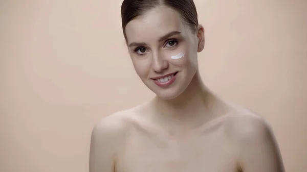 Cheerful young woman with bare shoulders and face cream isolated on beige — Fotografia de Stock