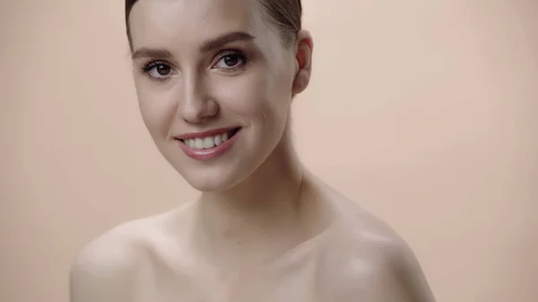 Mujer joven positiva con maquillaje y hombros desnudos aislados en beige - foto de stock