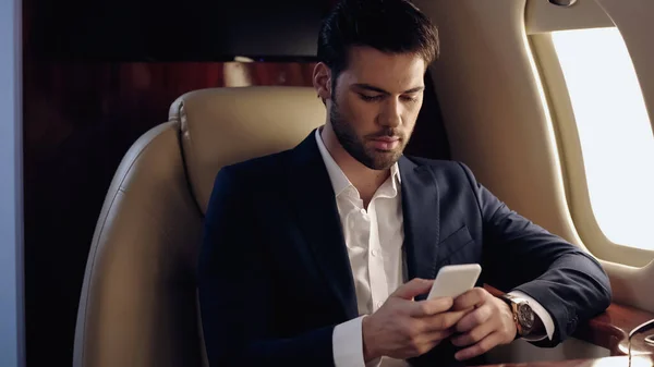 Businessman using smartphone in private plane — Stock Photo