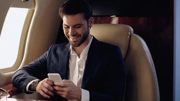 Hombre de negocios sonriente usando el teléfono celular en un avión privado - foto de stock