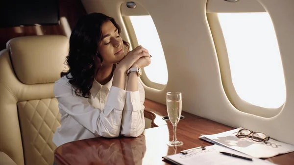 Young businesswoman sitting near contract, champagne and newspaper in private plane — Stock Photo