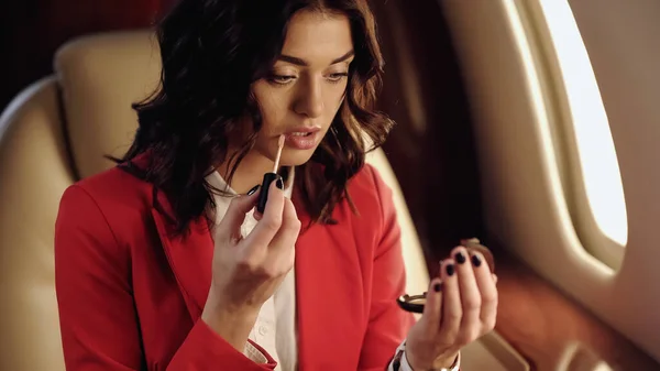 Businesswoman applying lip gloss and holding mirror in private plane — стоковое фото