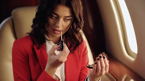 Businesswoman applying lip gloss and holding mirror in private jet — стоковое фото