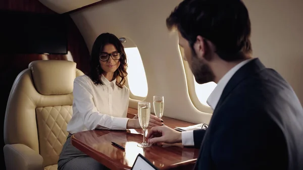 Businesswoman taking glass of champagne near blurred boyfriend in private plane — Stock Photo