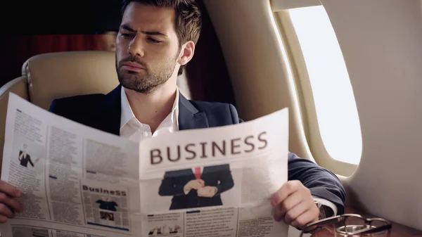 Businessman reading newspaper near eyeglasses in private plane — Fotografia de Stock