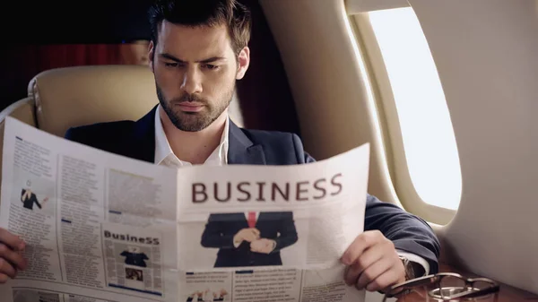 Bearded businessman reading news near eyeglasses in private plane — Stock Photo