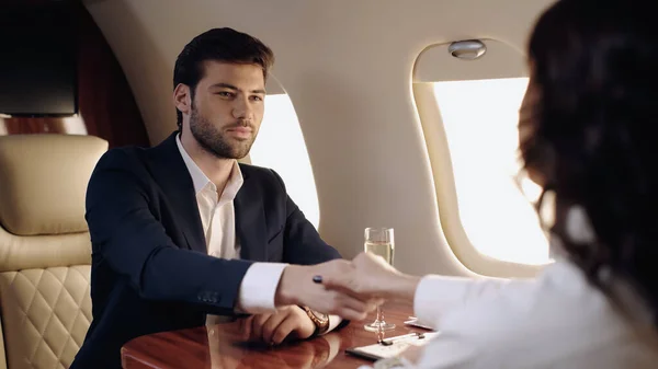 Businessman shaking hands with blurred colleague near champagne in private jet — Stock Photo