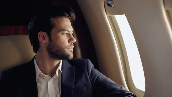 Bearded businessman looking at window in private plane — Foto stock