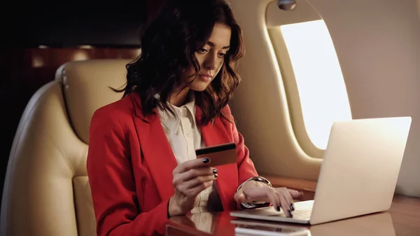Empresaria usando laptop y sosteniendo tarjeta de crédito en avión privado - foto de stock