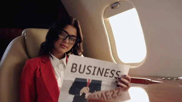 Businesswoman in eyeglasses reading newspaper in private jet — стоковое фото