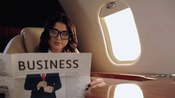 Young businesswoman in eyeglasses reading news in private plane — стоковое фото