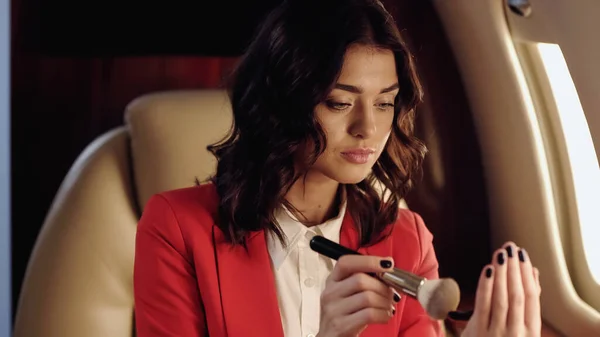 Businesswoman holding cosmetic brush and mirror in private plane — Stock Photo