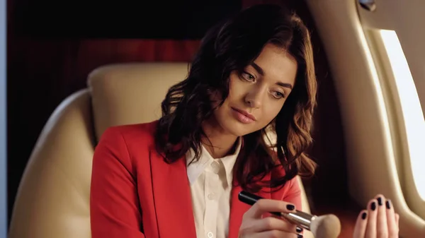 Young businesswoman holding cosmetic brush in private plane — Stock Photo