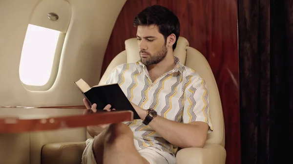 Bearded man reading book in private plane — Stock Photo