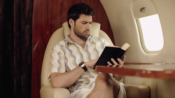 Бородатий чоловік читає книгу під час подорожі в приватному літаку — стокове фото
