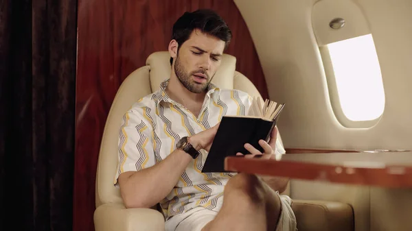 Focused bearded man reading book near table in private jet — стоковое фото