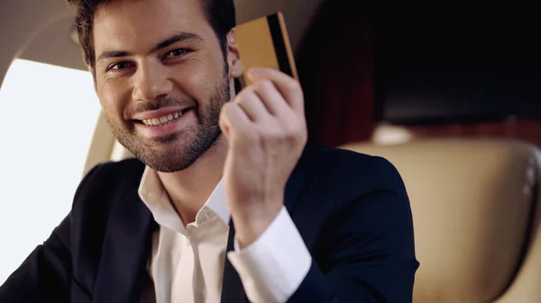 Усміхнений бізнесмен тримає кредитну картку в приватному літаку — стокове фото