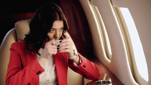 Businesswoman drinking coffee and looking at window in private plane — Stock Photo