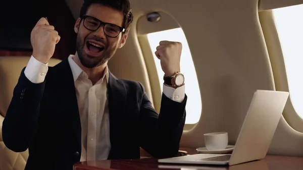 Excited businessman sitting near laptop and coffee in private plane — Stock Photo