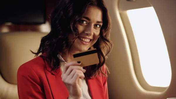 Cheerful businesswoman holding credit card in private plane - foto de stock