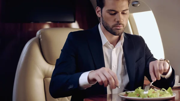 Бізнесмен тримає столові прибори біля розмитого свіжого салату в приватному літаку — стокове фото
