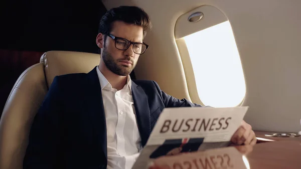 Businessman in eyeglasses holding blurred newspaper in private plane — Fotografia de Stock