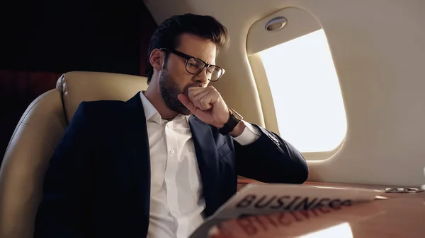 Businessman yawning near newspaper in private plane — Stock Photo