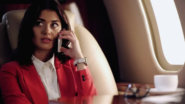 Businesswoman talking on cellphone near blurred cup in private plane — Stock Photo