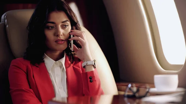 Upset businesswoman talking on smartphone near cup in private plane — Stock Photo