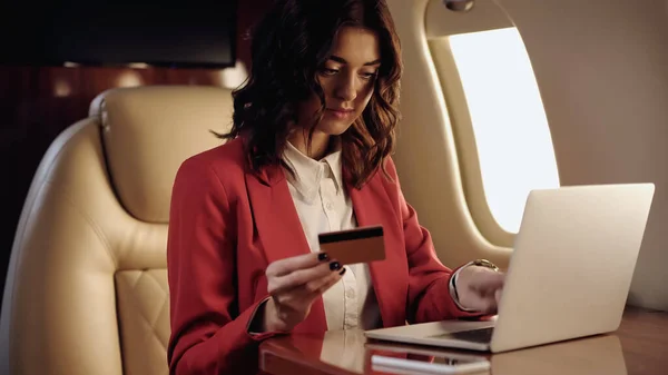 Joven empresaria con tarjeta de crédito cerca de dispositivos borrosos en avión privado - foto de stock