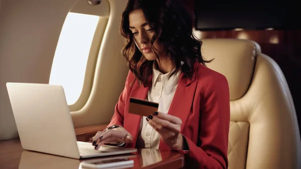 Businesswoman holding credit card and using laptop near cellphone in private jet — Fotografia de Stock