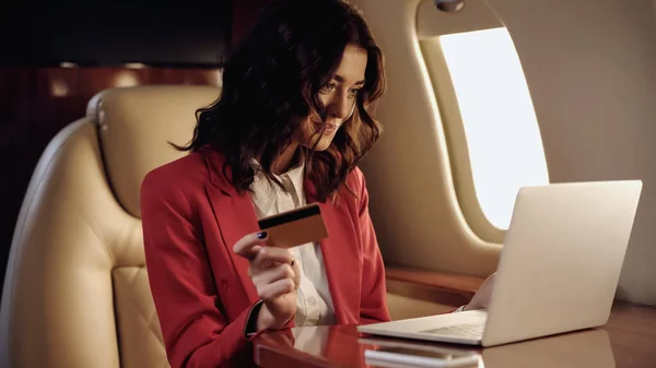 Smiling businesswoman using credit card and laptop in private plane — Stock Photo