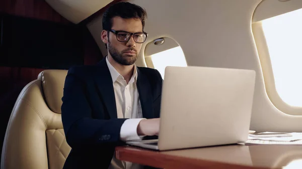 Businessman using laptop near cellphone and papers in private plane — Stock Photo