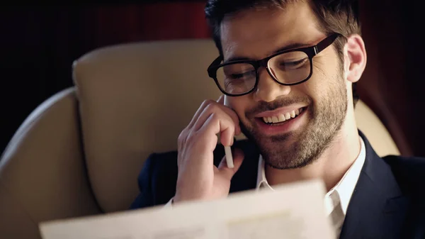 Smiling businessman talking on cellphone and reading newspaper in private jet — Stock Photo