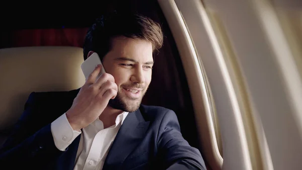 Hombre de negocios sonriendo mientras habla en el teléfono inteligente en avión privado - foto de stock