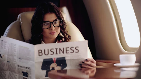 Businesswoman reading newspaper near blurred cup of coffee in private plane — Stock Photo