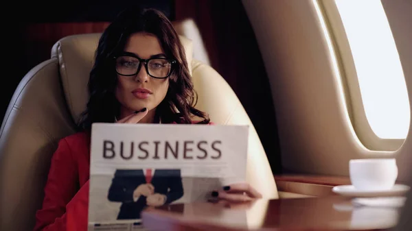Young businesswoman reading blurred newspaper near cup in private plane — Fotografia de Stock