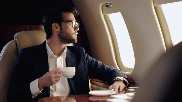 Homme d'affaires barbu tenant une tasse dans un avion privé — Photo de stock