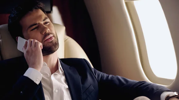 Businessman in suit talking on smartphone in private plane — Stock Photo