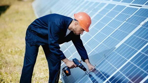Engenheiro em hardhat usando broca elétrica perto de painéis solares modernos — Fotografia de Stock