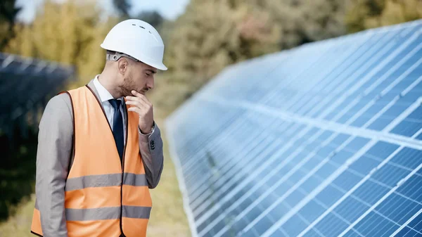 Pensive businessman in safety vest and hardhat looking at solar panels — Stock Photo