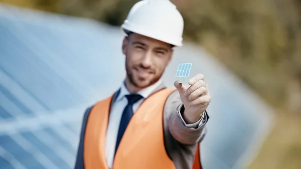 Uomo d'affari sfocato e sorridente che mostra piccolo modello di batteria solare — Foto stock