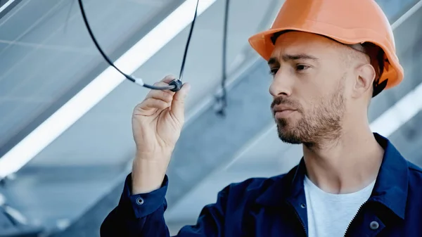 Engineer in hardhat checking wire of solar panel — Stock Photo