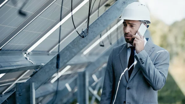 Homem de negócios triste olhando para o fio pendurado enquanto conversa no smartphone perto de painéis solares — Fotografia de Stock