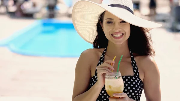 Fröhliche junge Frau in gepunktetem Badeanzug und Strohhut mit Glas und Cocktail — Stockfoto