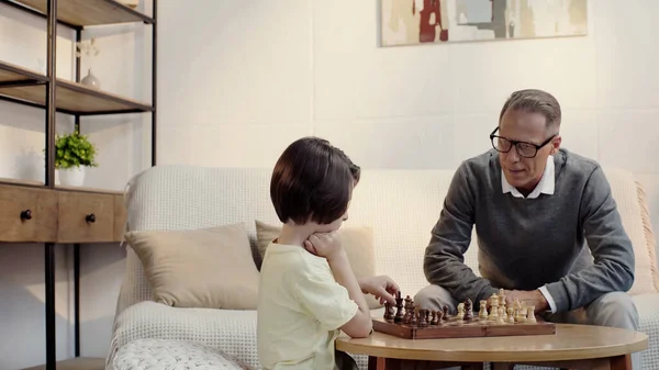 Grandfather and smart grandson playing chess in living room — Photo de stock