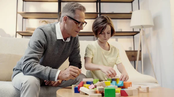 Middle aged grandfather in glasses playing building blocks with preteen boy — Stock Photo