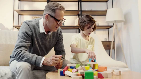 Middle aged grandfather in glasses playing building blocks with boy — Stockfoto
